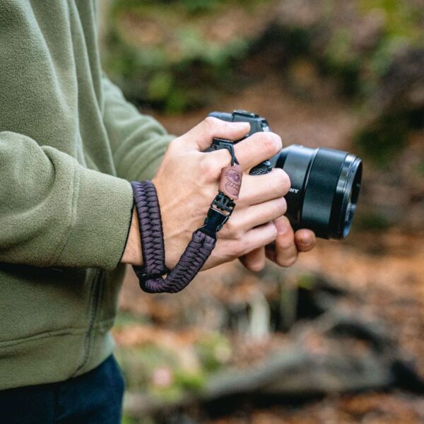 Abgebildet ist eine Person, die ihre Kamera mit der The Claw Handschlaufe von C-Rope in der Farbe Dark Coffee gesichert hat.
