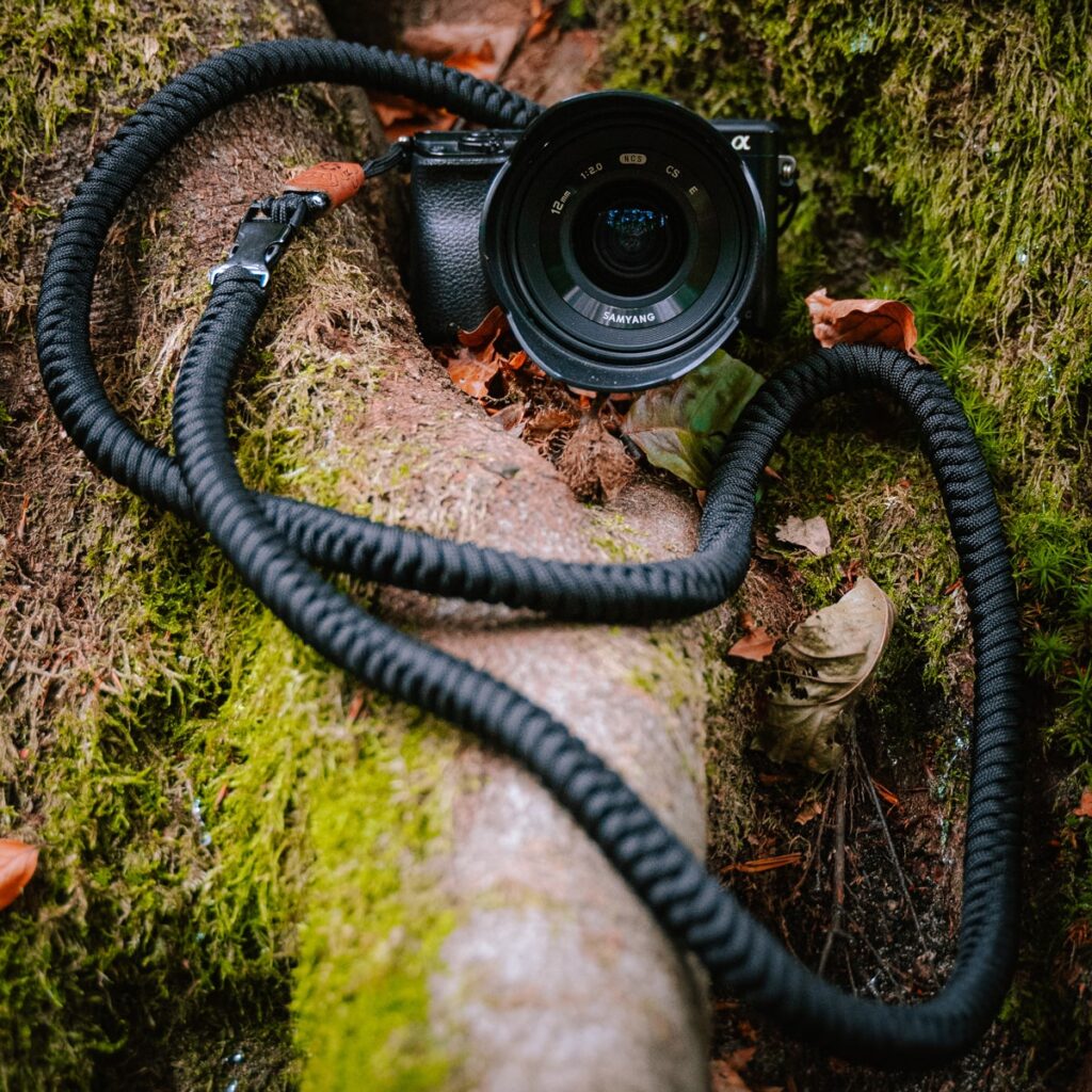Das Bild zeigt eine im Wald platzierte Kamera, an der der C-Rope Kameragurt The Urbanist in Silent Black befestigt ist.