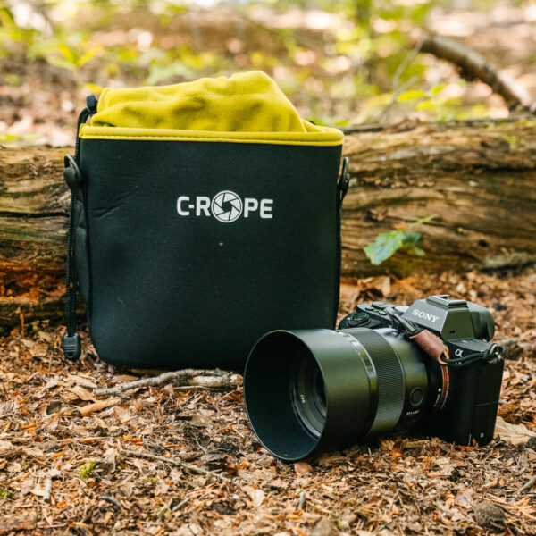 Hier zu sehen ist ein C-Rope Kamerabeutel der Größe M im Wald, mit einer danebenliegenden Kamera.