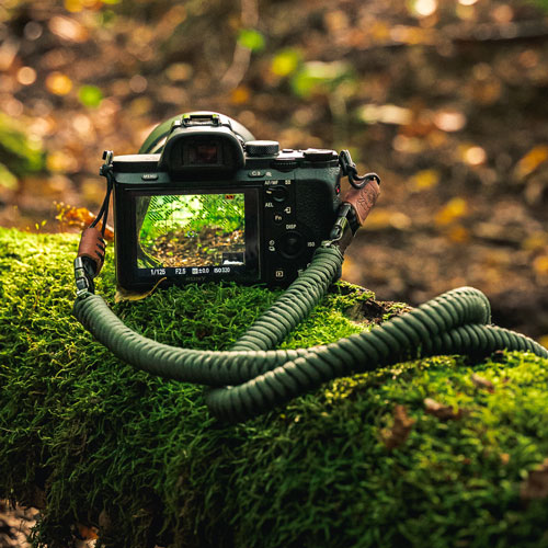 Man sieht eine Kamera im Wald, an der der Kameragurt The Urbanist in der Farbe Military Olive befestigt ist.
