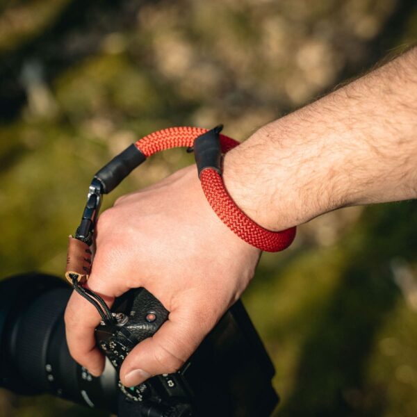Mann trägt Kamerahandschlaufe aus Kletterseil in der Natur in der Farbe bright red.