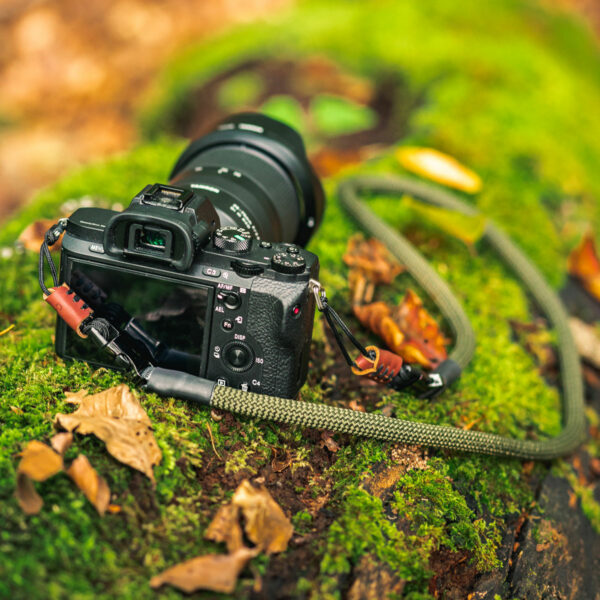 Auf dem Bild abgebildet ist eine Kamera auf einem Baumstamm, an der der Kameragurt aus Kletterseil in der Farbe Military Olive befestigt ist.
