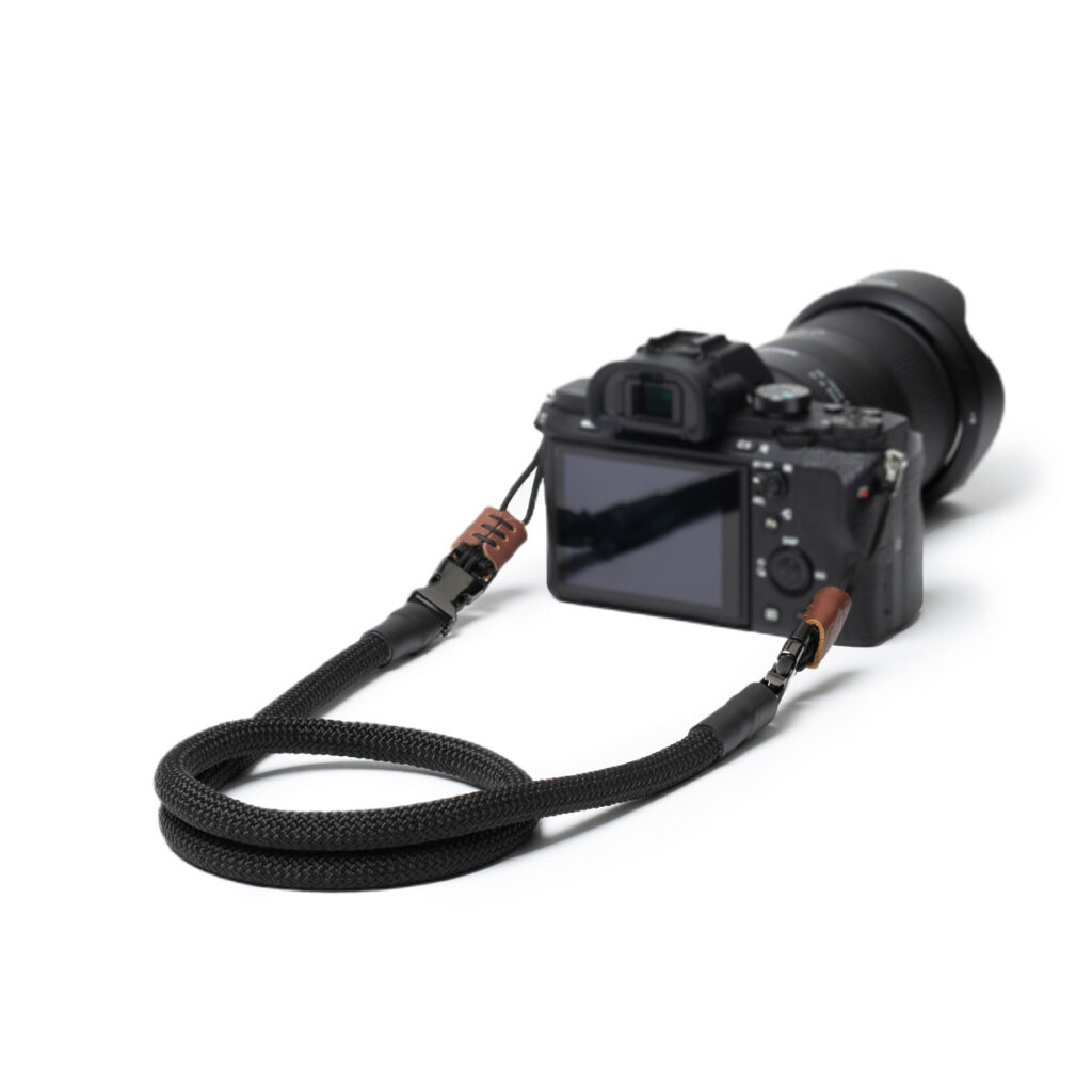 Das Bild zeigt eine Kamera mit dem C-Rope Kameragurt in Seil-Form in der Farbe Black Hero.