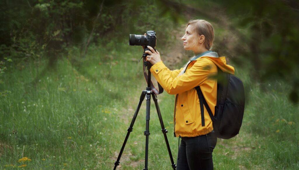 Zu sehen ist eine Frau im Wald mit einer Kamera auf einem Stativ.